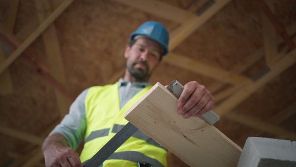 Carpenter working on buidling site of wooden eco house wearing safety vest and helmet.