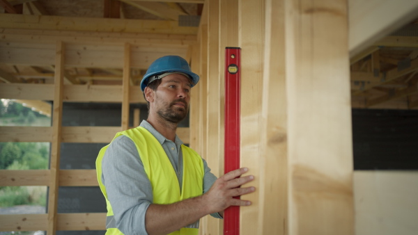 Carpenter working on buidling site of wooden eco house, using spirit level.