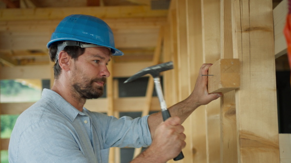 Carpenter working on building site of sustainable wooden house using a hammer.