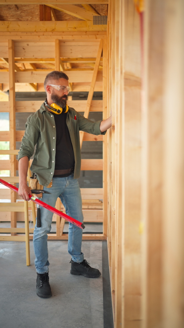 Carpenter working on buidling site of wooden eco house, measuring wooden wall.