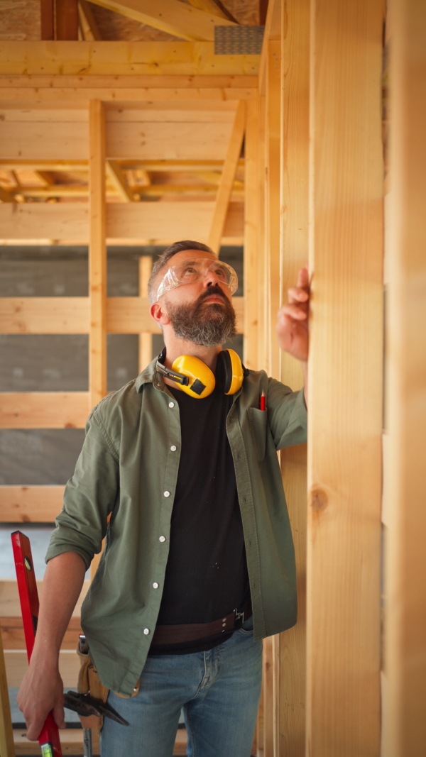 Carpenter working on buidling site of wooden eco house, measuring wooden wall, using a spirit level tool. vertical shot.