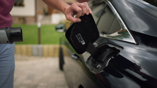 Close up of man charging electric car in driveway.