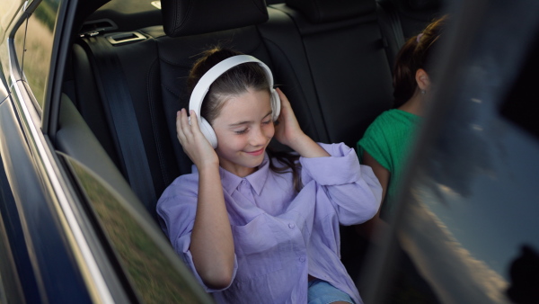 Girl sitting in backseat of car, listening to music on headphones, swinging to the sound, smiling.