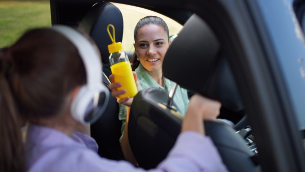 Caring mother in car handing a bottle of water and an apple to kids in backseat, while travelling.