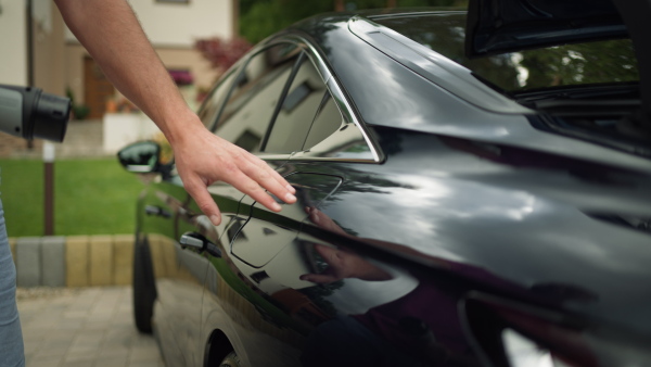 Close up of man opening lid on black car, inserting the charger.