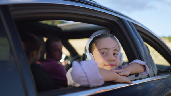 Girl with headphones leaning out of car window, listening to music, enjoying the sunset.