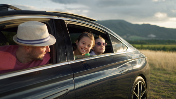 Girl leaning out of car window, on family trip, smiling, looking into camera, enjoying the sunset.