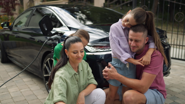 Family taking selfie in front of electric car while charging it in front of their house.