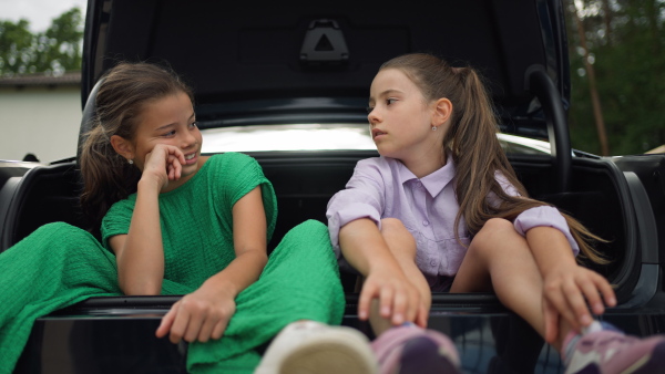 Two sisters sitting in open car trunk, talking seriously.