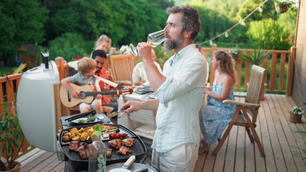 A man grilling ribs and vegetable on grill during family summer garden party, close-up