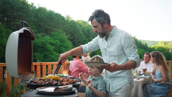 A man grilling ribs and vegetable on grill during family summer garden party, close-up