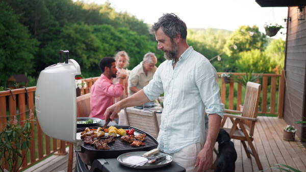 A man grilling ribs and vegetable on grill during family summer garden party, close-up