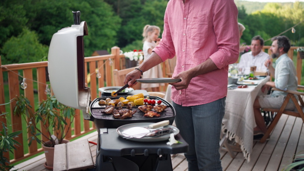 A man grilling ribs and vegetable on grill during family summer garden party, close-up