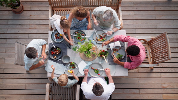 A top view of 3 generations family eating at barbecue party dinner on patio, people sitting on patio with grill.