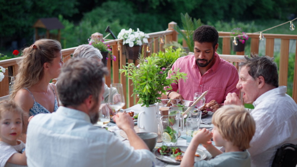 Three generations family having fun at barbecue party dinner on patio, people sitting at table on patio with grill.