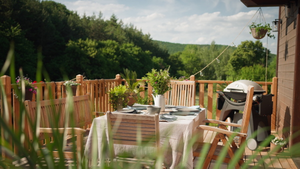 A dining table with wooden chairs set for dinner on the terrace with grill in summer, garden party. concept.