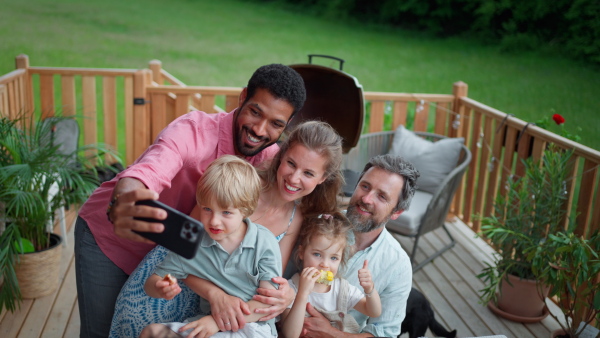 A family with kids having fun at barbecue party dinner on patio, people sitting and taking selfie.