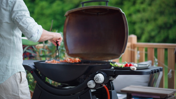 An unrecognizable man grilling ribs and vegetable on grill during family summer garden party