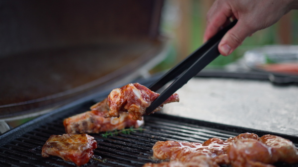 An unrecognizable man grilling ribs on grill during family summer garden party, close-up