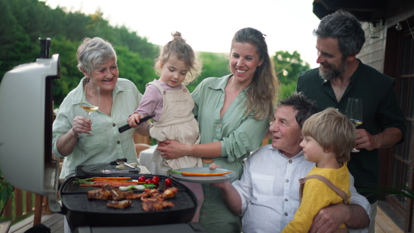 A multi generation family grilling outside on patio in summer during garden party