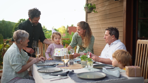 A multi generation family celebratiing birthday of little girl and having garden party outside on patio.