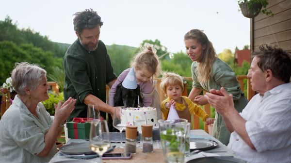 A multi generation family celebratiing birthday of little girl and having garden party outside on patio.