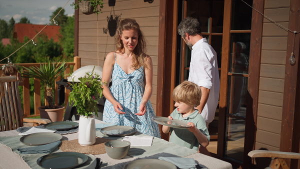 Happy kids helping a mother to lay up the table at the summer patio, family lifestyle