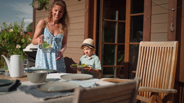 A happy kid helping mother to lay up the table at the summer patio, family lifestyle