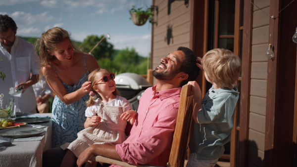 A family with kids having fun at barbecue party dinner on patio, people sitting at table on patio and talking