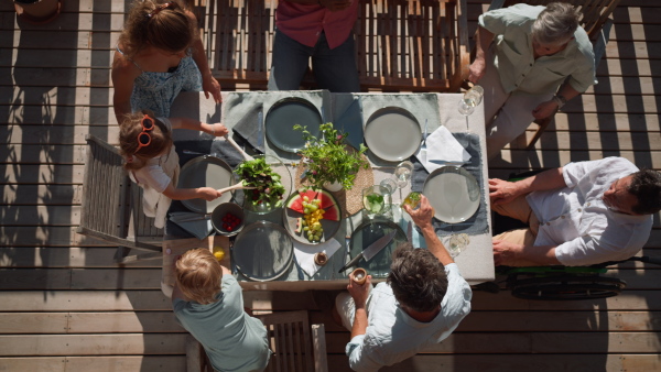 A top view of 3 generations family eating at barbecue party dinner on patio, people sitting on patio with grill.