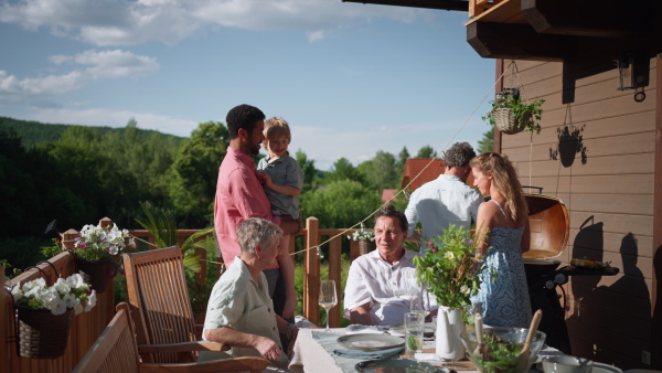 Three generations family having fun at barbecue party dinner on patio, people sitting at table on patio with grill.