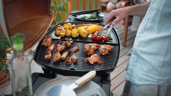 An unrecognizable man grilling ribs and vegetable on grill during family summer garden party