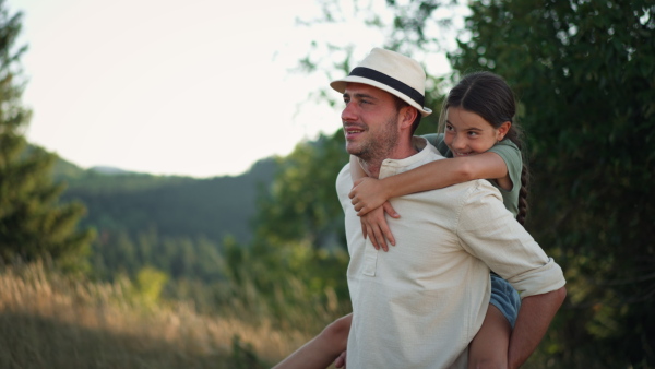 A happy father giving his daughter piggyback ride in summer in nature.