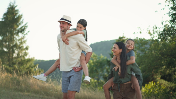 Happy parents giving their children a piggyback ride in summer in nature.