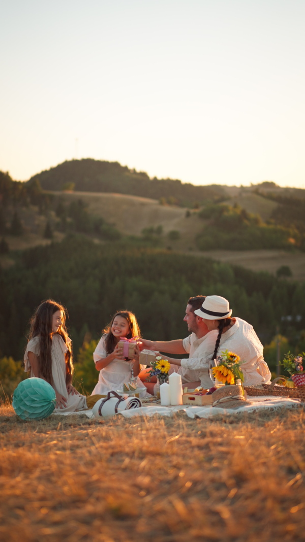 A happy family with children celebrating birthday with gifts outdoors on a picnic in park. Vertical footage.