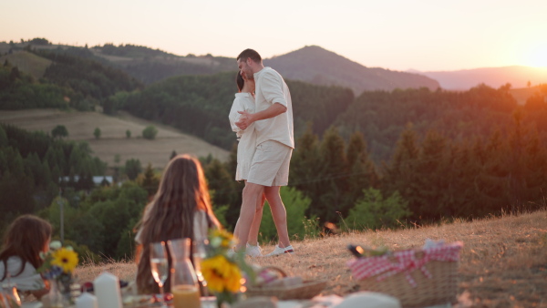 Family with children having picnic in the nature, enjoying sunset. Parents dacing in front of children.