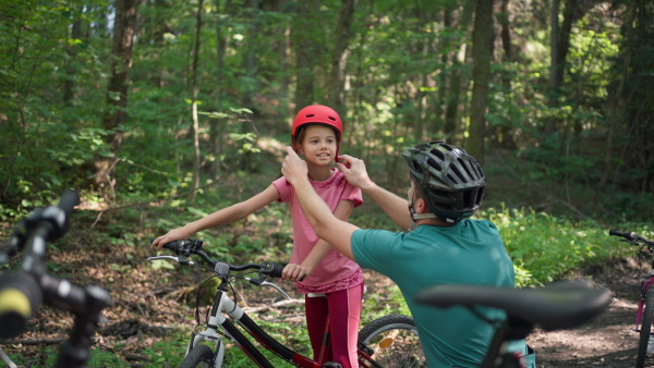 A young father with little daughter preapring for bike ride, standing with bicycles in nature.