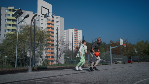 A happy father and teen daughter playing basketball outside at court.