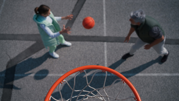 A father and teenage daughter playing basketball outside at court, high angle view above hoop net.