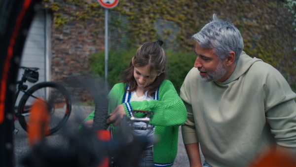 A happy father with teenage daughter repairing bicycle in street in town.