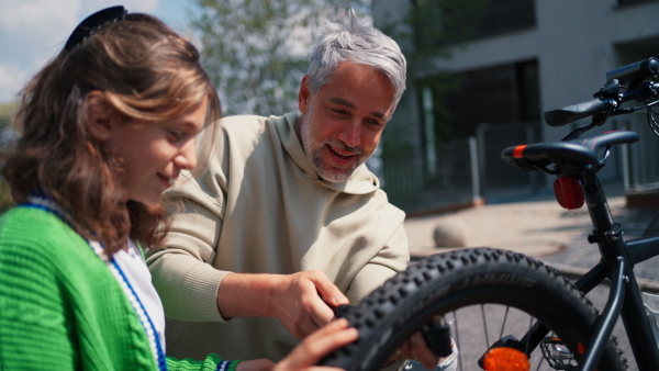 A happy father with teenage daughter repairing bicycle in street in town.