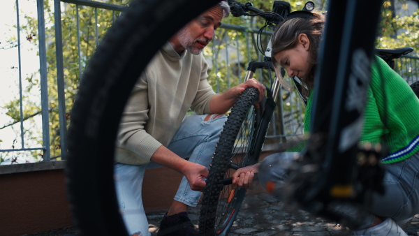 A happy father with teenage daughter repairing bicycle in street in town.