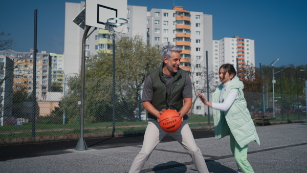 A happy father and teen daughter playing basketball outside at court.