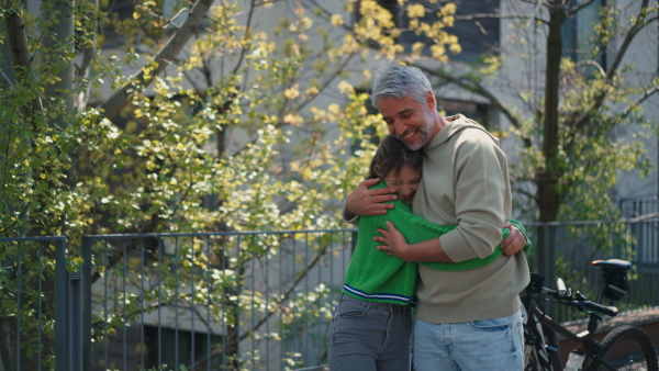 A teenage daughter hugging her father outside in town when spenidng time together.