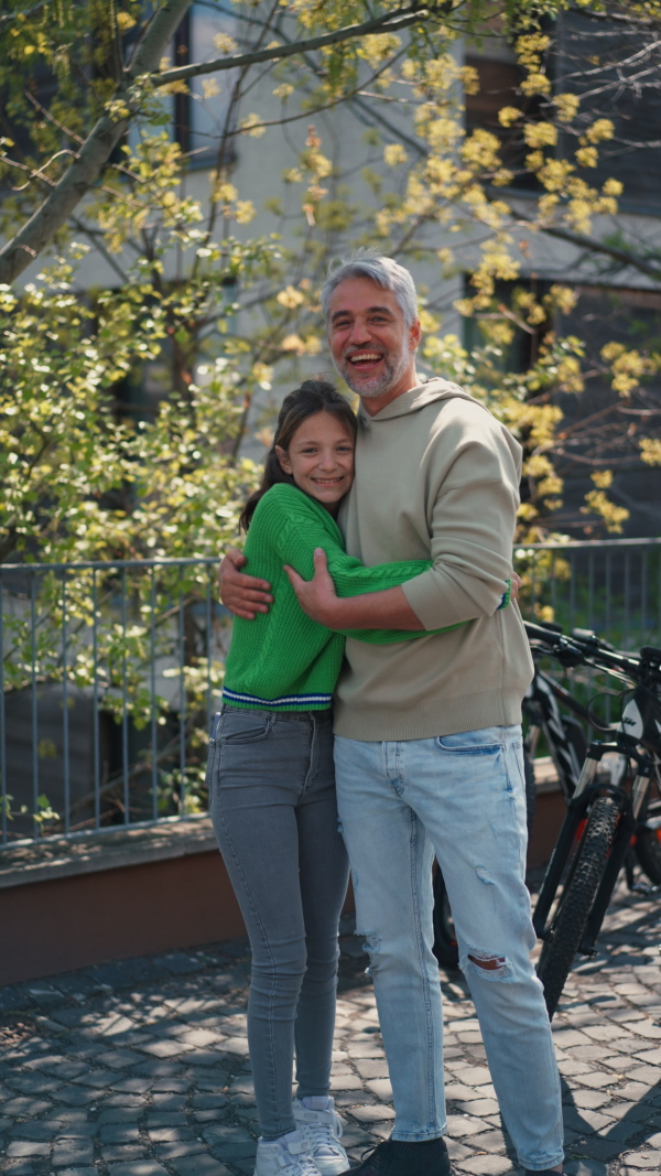 A teenage daughter hugging her father outside in town when spenidng time together.