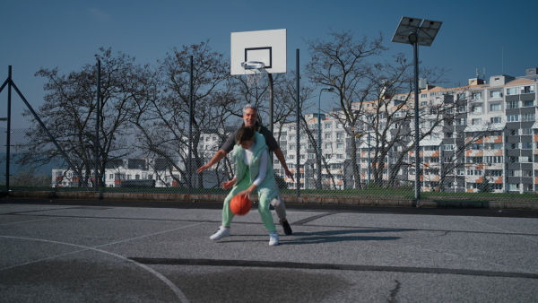 A happy father and teen daughter playing basketball outside at court.