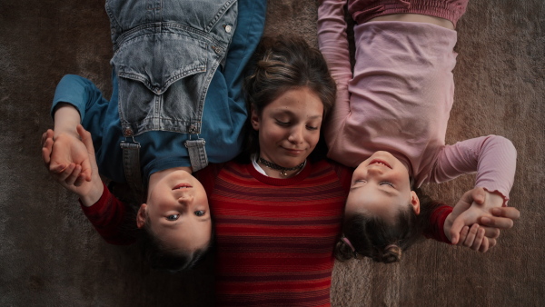 A top view of happy three sisters kids lying on floor and looking at camera.