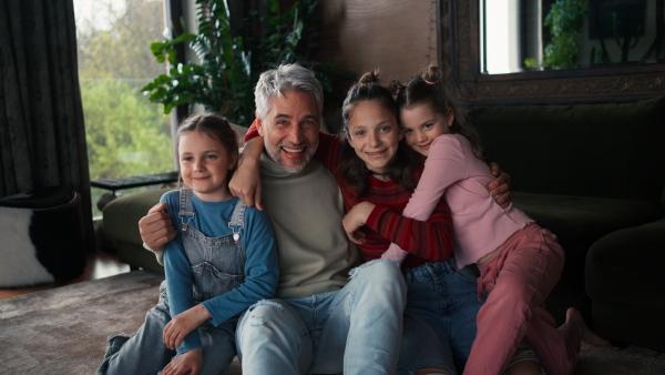 Three little daughters hugging their father at home.