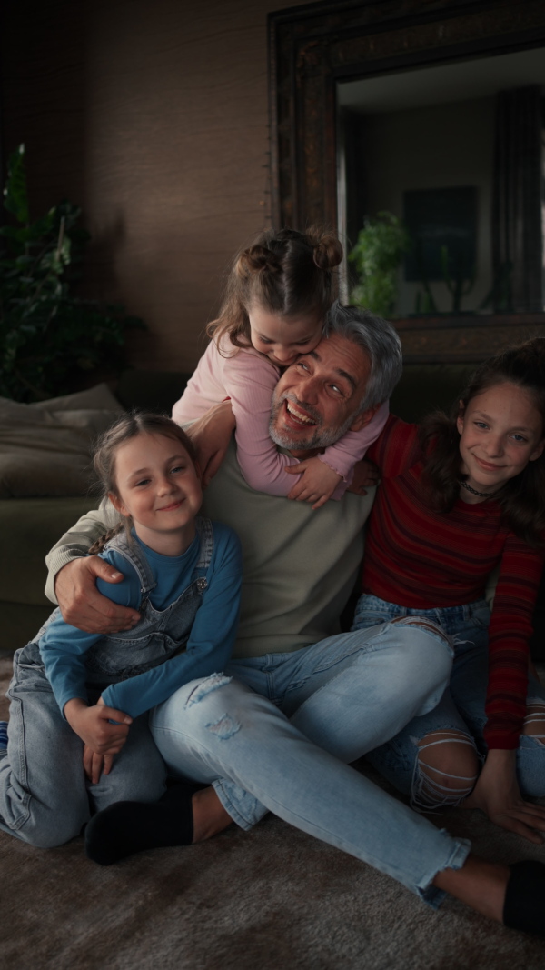 A vertical footage of three little daughters hugging their happy father at home.