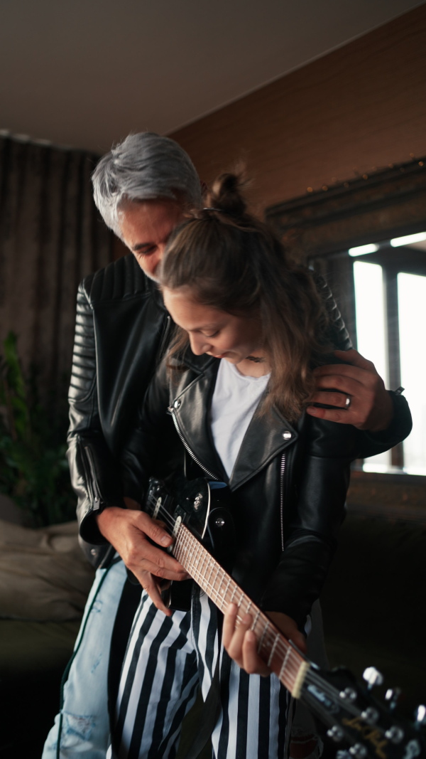 A vertical footage of father rock guitarist having fun and and dancing with his teenage daughter at home.